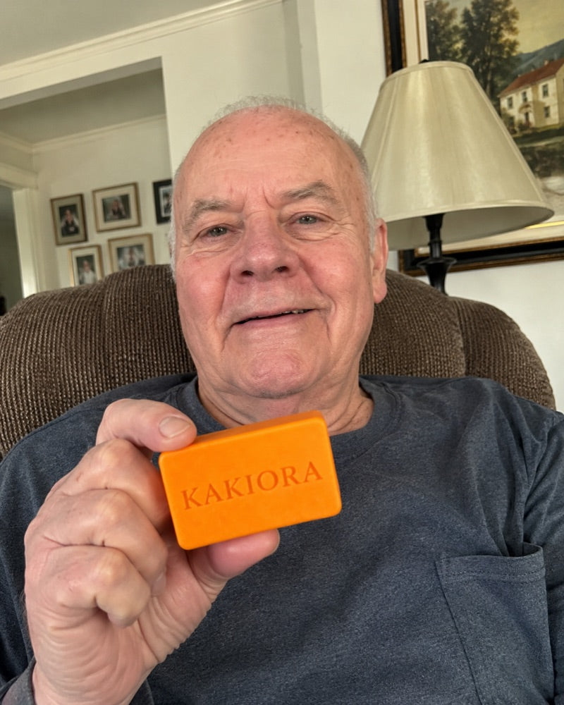 Older man holding a bar of KAKIORA persimmon soap in his living room