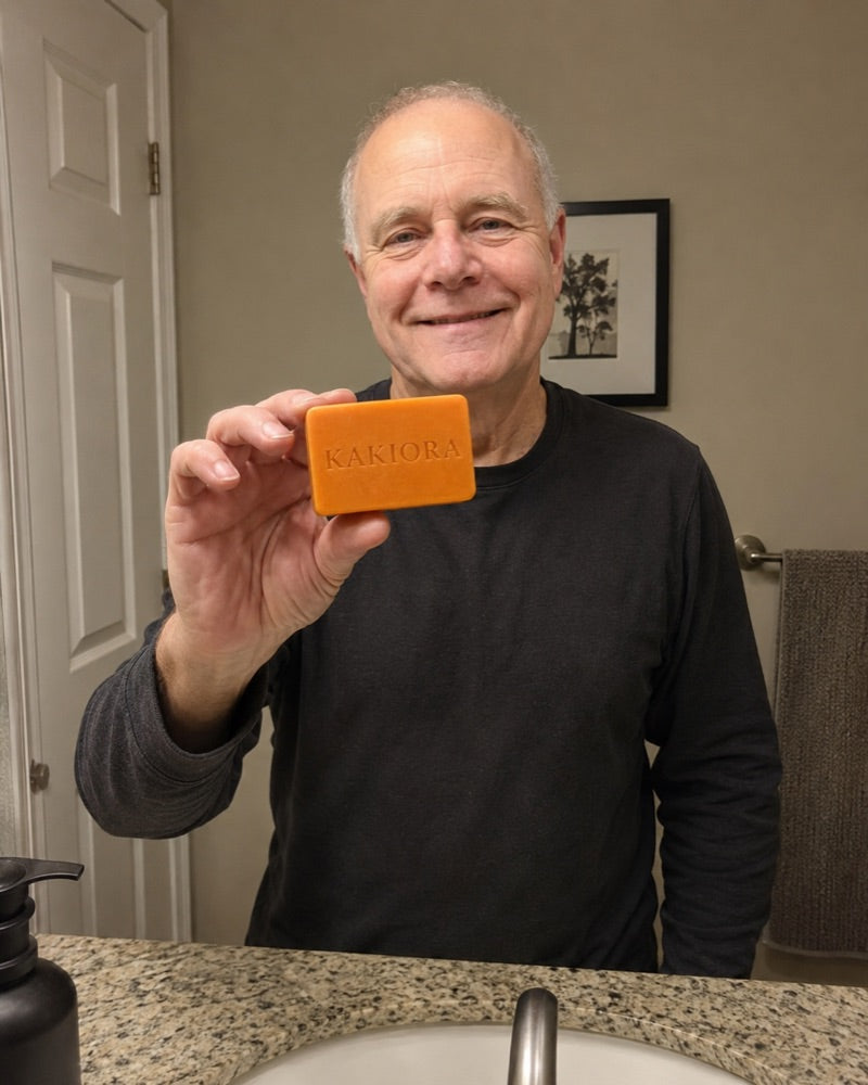 Older man at the bathroom sink holding a bar of KAKIORA persimmon soap